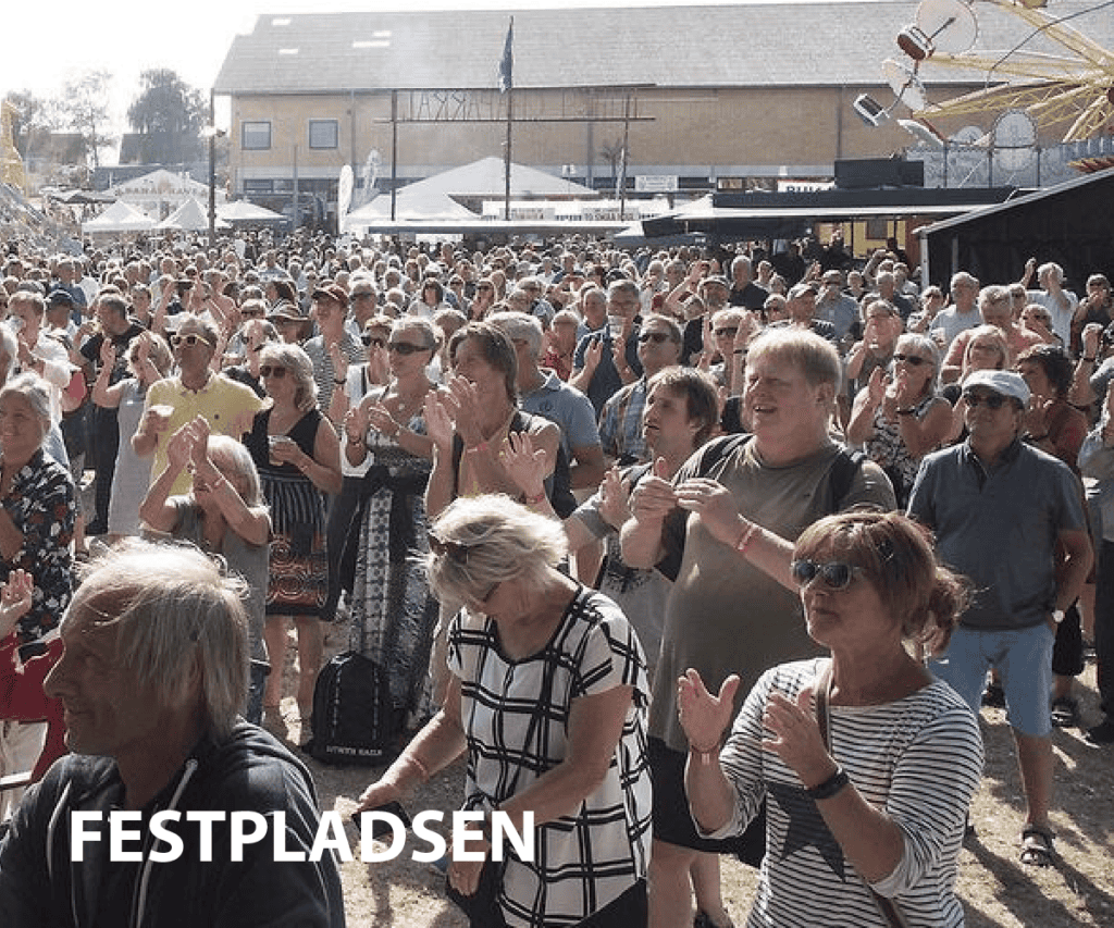 Folk danser og nyder Bakkefest på festivalpladsen i solskin.